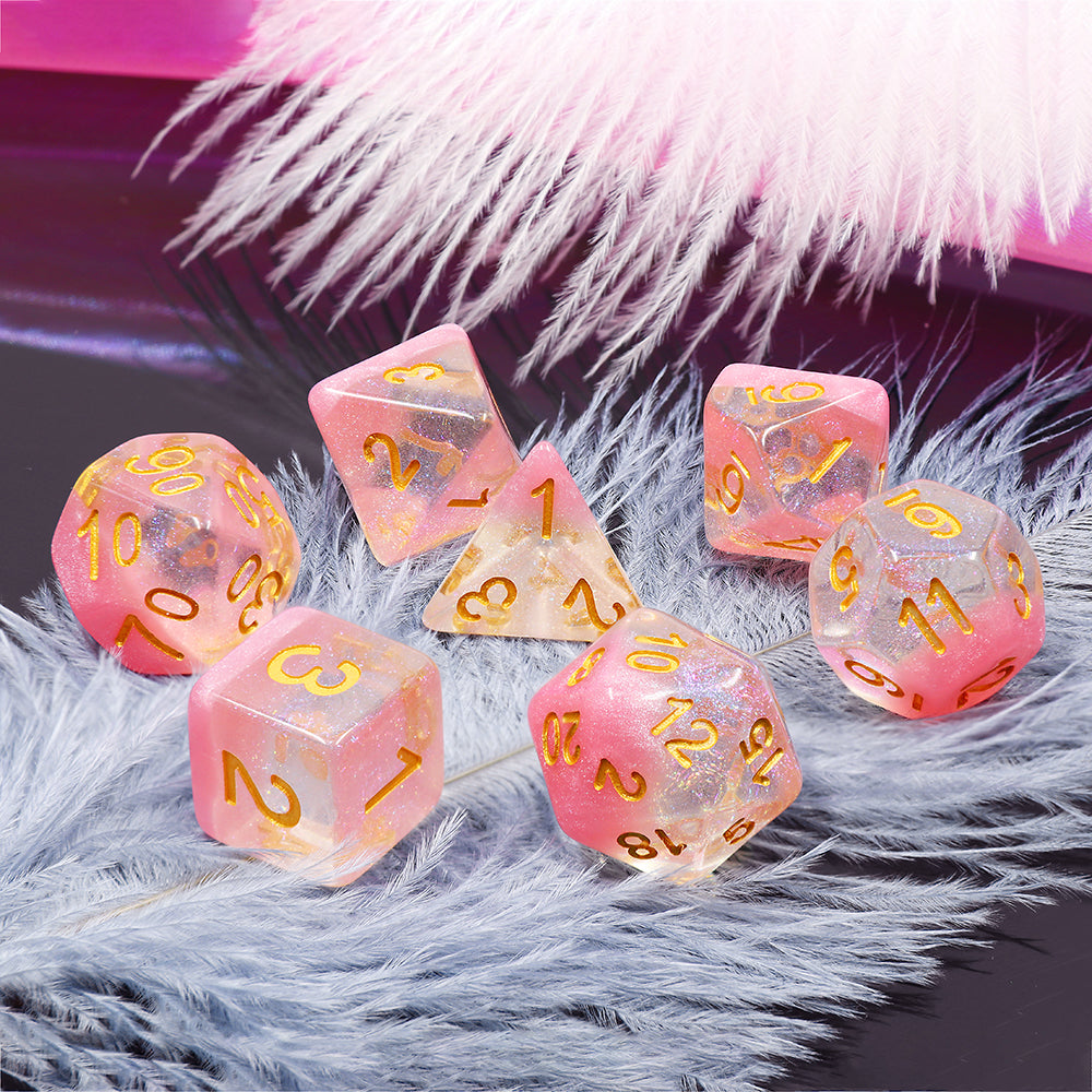 A set of pink polyhedral dice with golden font, placed on a fluffy surface. The dice are of various shapes including a tetrahedron, cube, octahedron, dodecahedron, and icosahedron, representing a complete set for board games like Dungeons and Dragons.